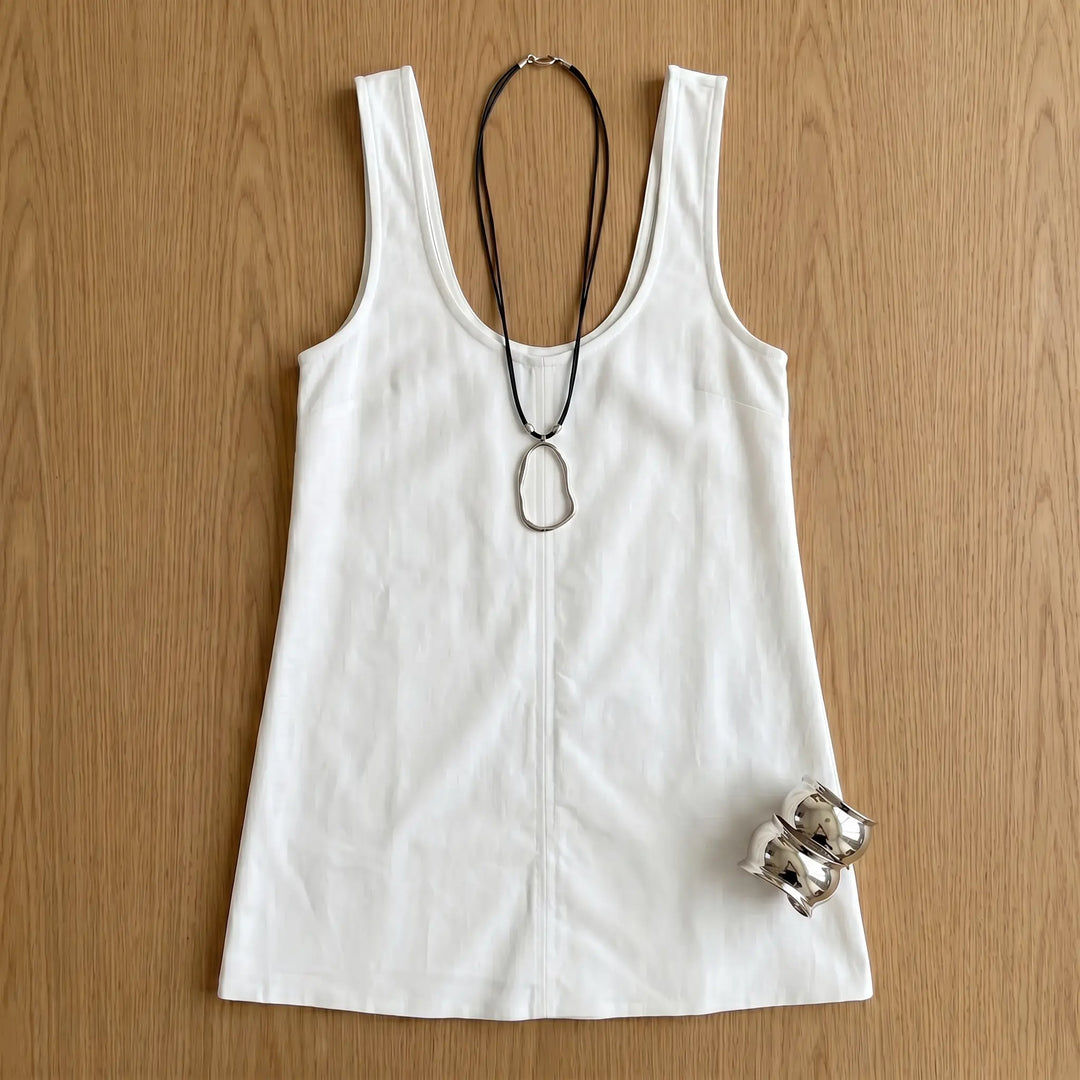 A sleeveless white A-line mini dress with a U-neckline and prominent center front seam, laid flat with styled silver necklace and bracelets.