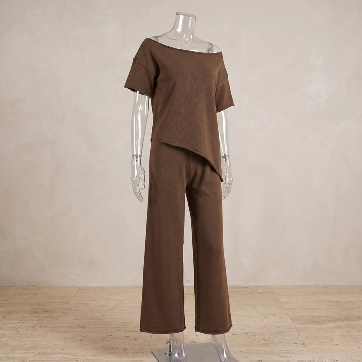 Brown ribbed knit loungewear set featuring an asymmetrical off-shoulder top with short frayed sleeves and wide-leg pants with a raw hem, displayed on a mannequin.