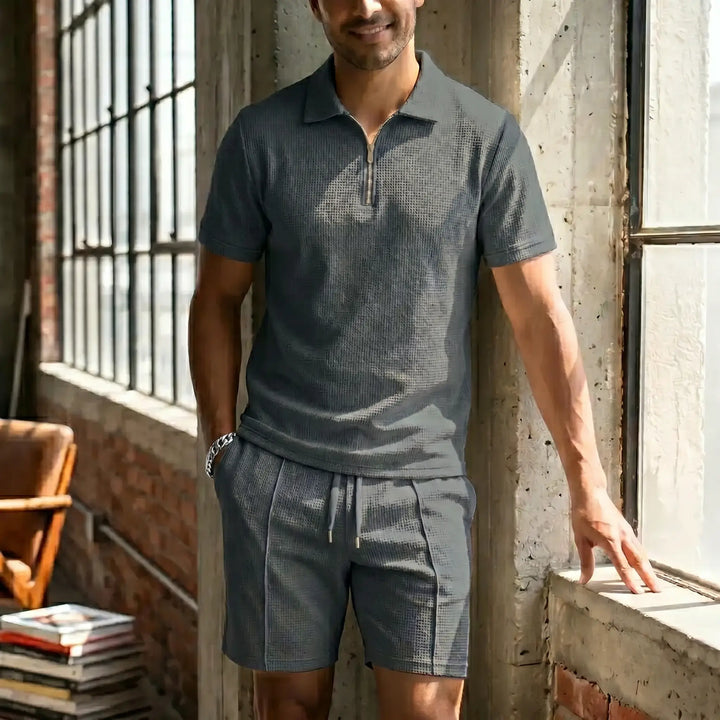 Man wearing a charcoal grey waffle knit loungewear set featuring a short-sleeve quarter-zip polo and drawstring shorts, posed in a relaxed indoor setting.