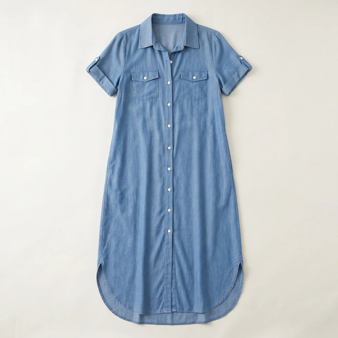 Medium blue wash denim shirt dress with a midi length, featuring a classic collar, short rolled sleeves, button-front closure, and two chest flap pockets, laid flat.