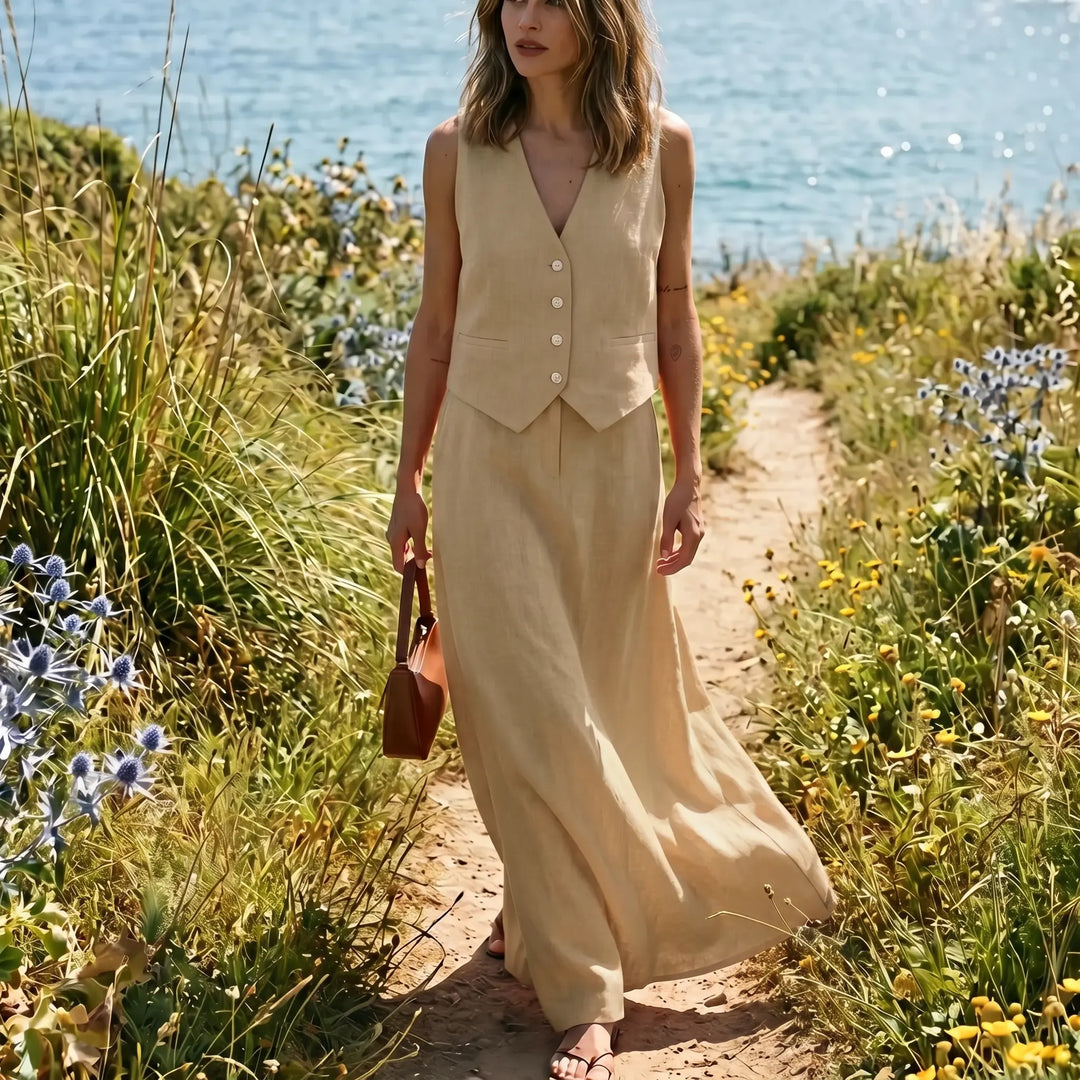 A woman walks on a coastal path wearing a soft khaki linen-cotton blend vest and flowing maxi skirt set, embodying effortless chic.