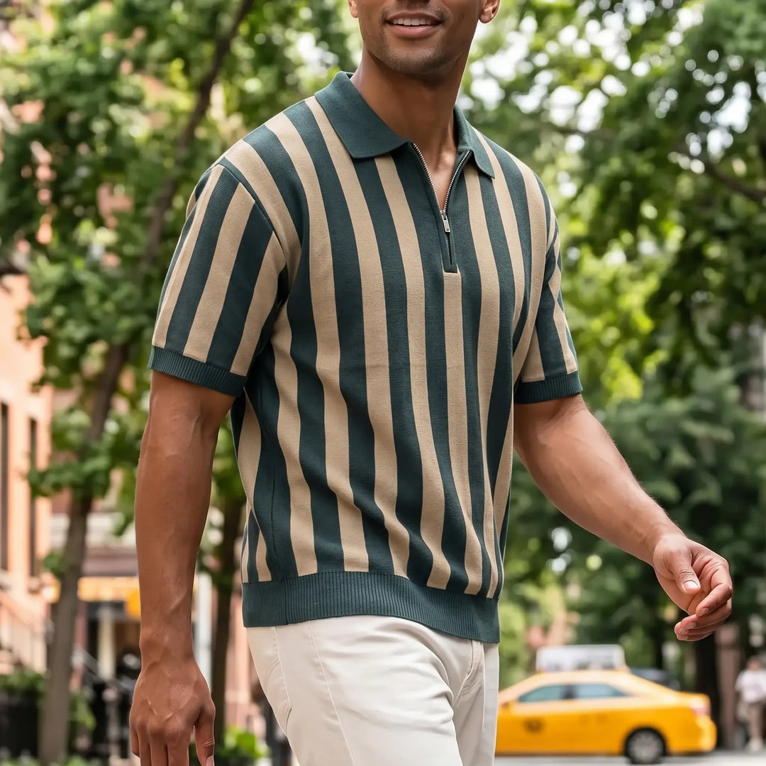 A man walks down a city street wearing a dark green and khaki striped short-sleeve knit polo shirt with a quarter-zip neckline and beige chinos.