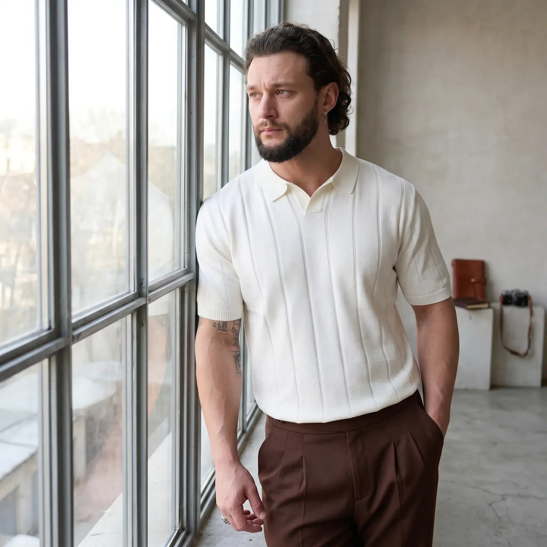 Men's white fine-gauge knit polo shirt with vertical ribbing, worn by a man looking out a window in a studio setting. Features short sleeves and a classic polo collar.