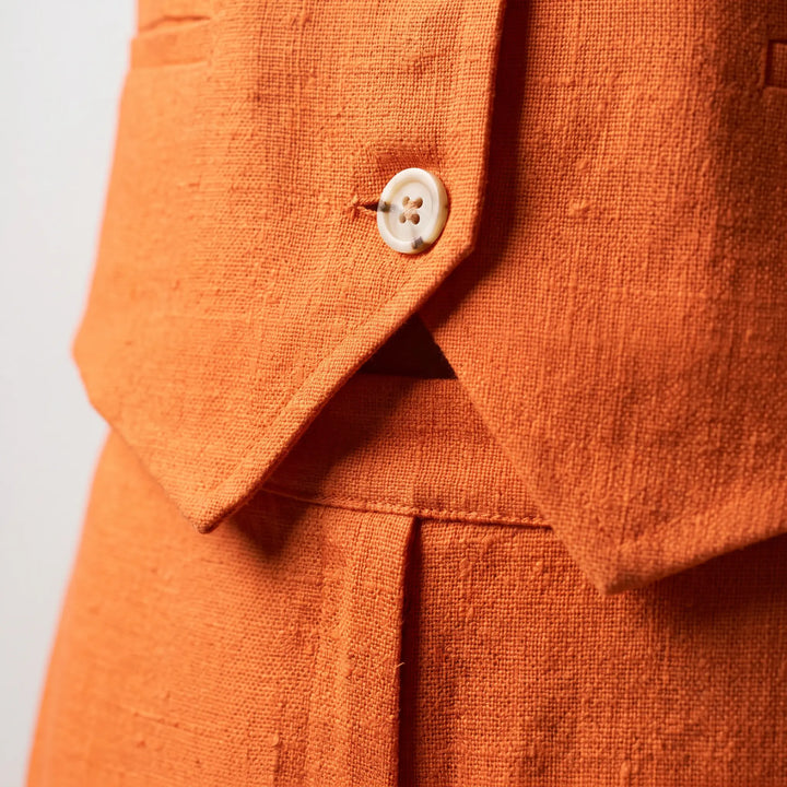 Close-up of vibrant marigold orange linen-cotton blend fabric, showcasing its natural slub texture and a single natural horn button on a sleeveless vest.