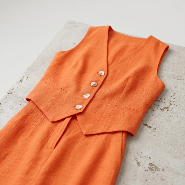Vibrant marigold orange linen-cotton blend set featuring a cropped sleeveless vest with V-neck and three natural buttons, paired with a high-waisted maxi skirt.