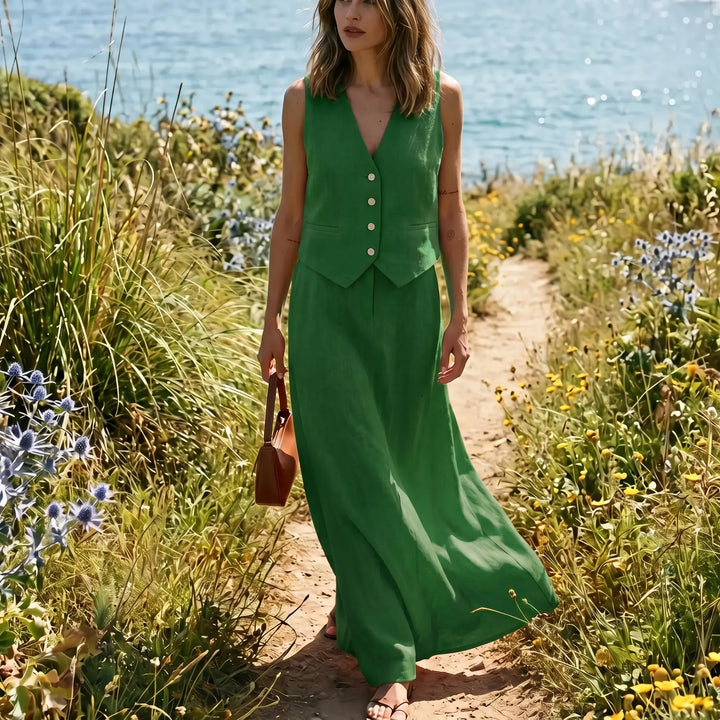 Vespera Forest Green linen-blend set featuring a cropped sleeveless vest and a high-waisted flowing maxi skirt, worn by a model on a scenic path by the sea.