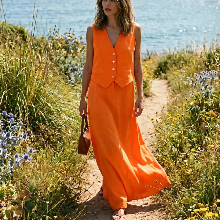 Vibrant marigold orange linen blend set with cropped vest and flowing maxi skirt, worn by a model walking along a coastal path.